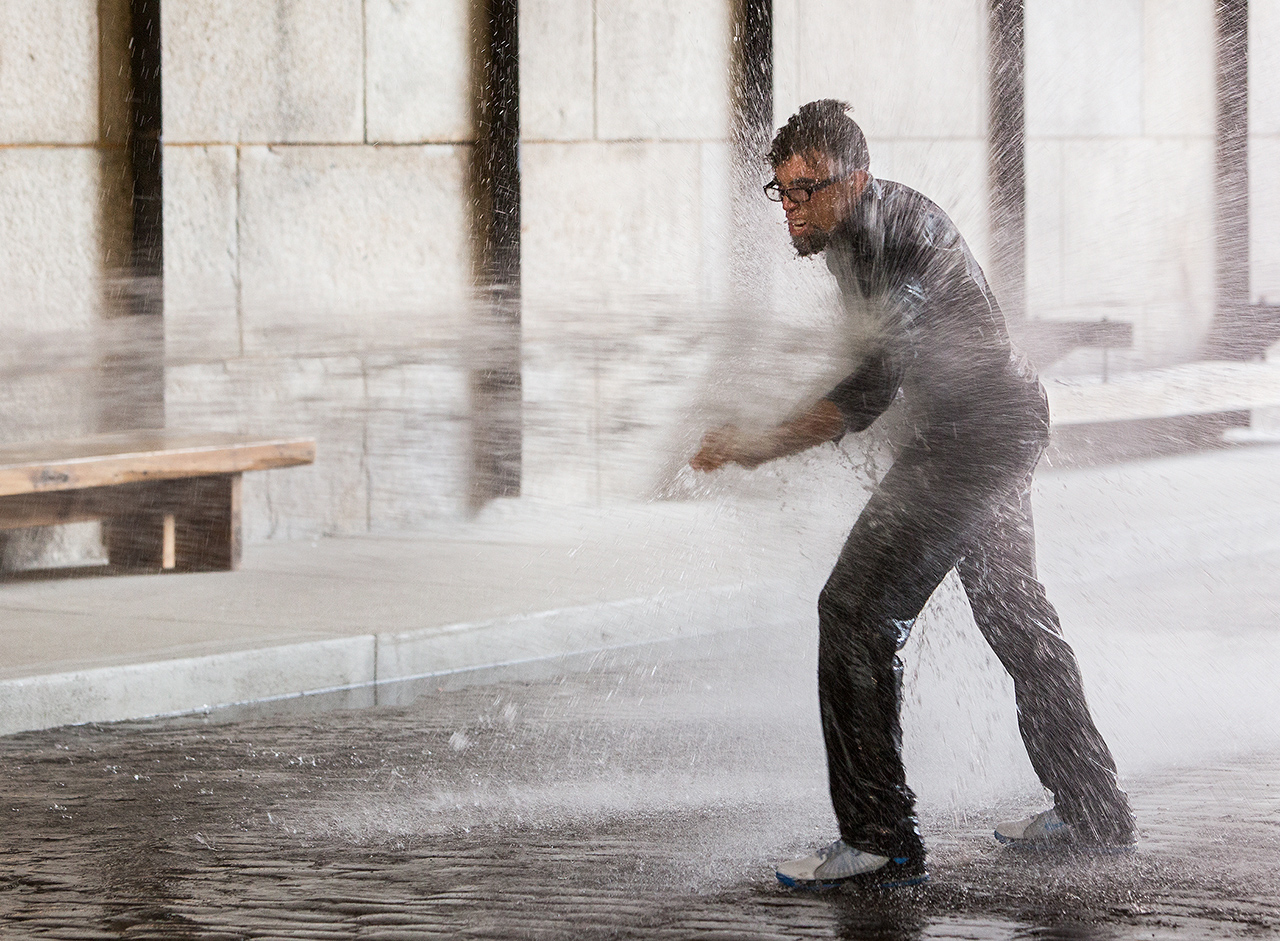 The artist walking against a the water from a firehose