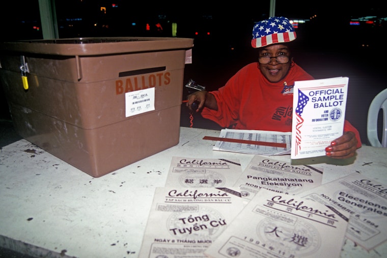 An election volunteer and a ballot box at a polling location, in California, in 2004. Photo credit: © Joe Sohm/Visions of America/Getty A woman sitting at a table with a ballot box