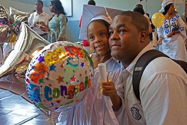 Young girl wearing cap and gown, and standing next to her father.
