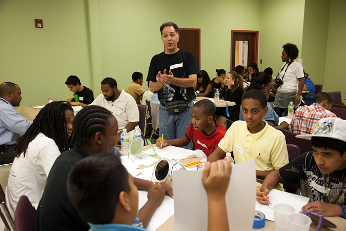 Jay Wolf Schlossberg-Cohen claps at a group of students in a classroom