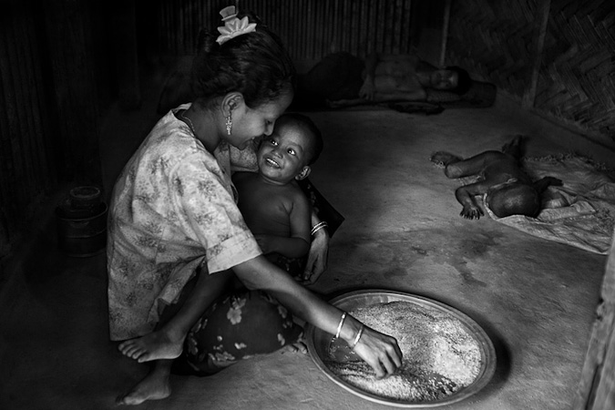 Woman holding baby while she prepares rice