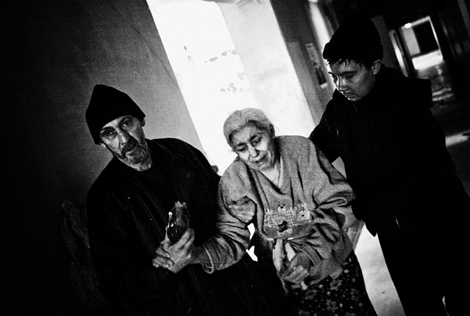 Two men assist an elderly woman as she walks