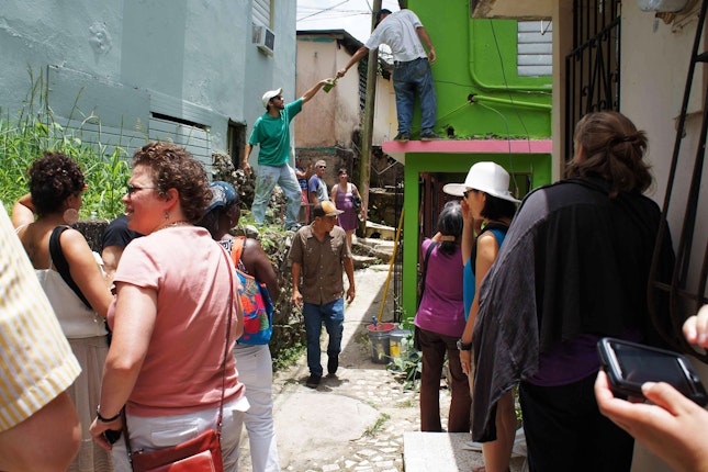 People walk through a neighborhood watching homes being painted.