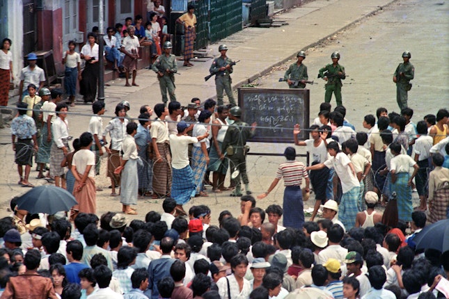 People and soldiers in a street around a chalkboard