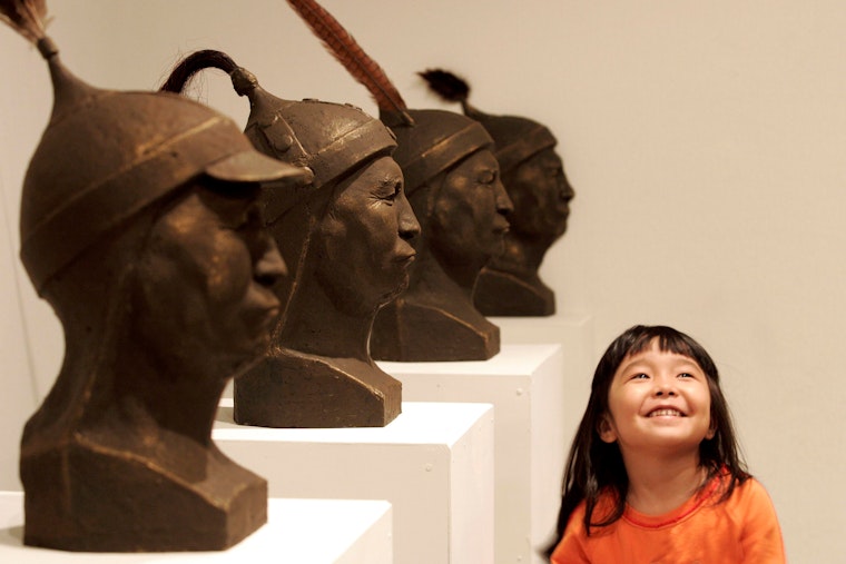 A young girl in a museum stands next to a row of sculpted heads.