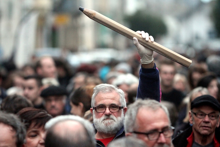 A man holding a giant pencil in the air in the middle of a crowd