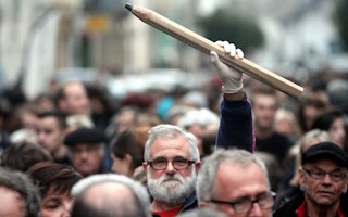 A man holding a giant pencil in the air in the middle of a crowd