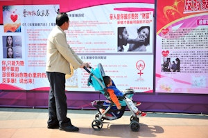 A man with a child in a stroller reading posters