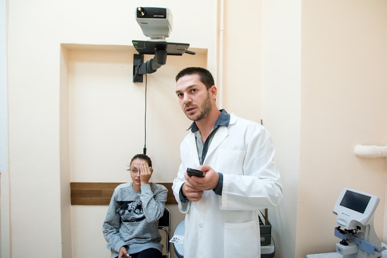 A doctor conduts an eye examination on a patient in a doctor's office.