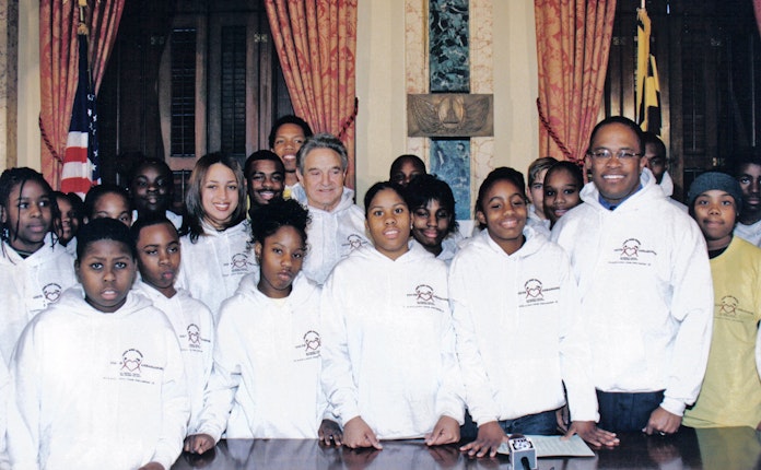 Students in matching sweatshirts pose for a photo with Kurt Schmoke and George Soros.