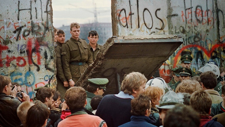 Soldiers standing behind a fallen section of the Berlin Wall