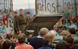 Soldiers standing behind a fallen section of the Berlin Wall