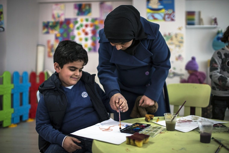 A child with autism paints and his mother paint together in a classroom at the Al-Farah Child and Family Support Center in Ankara, Turkey on February 21, 2017. Photo credit: © Özge Elif Kzl/Anadolu Agency/Getty A child and a woman in a classroom using a paintbrush.