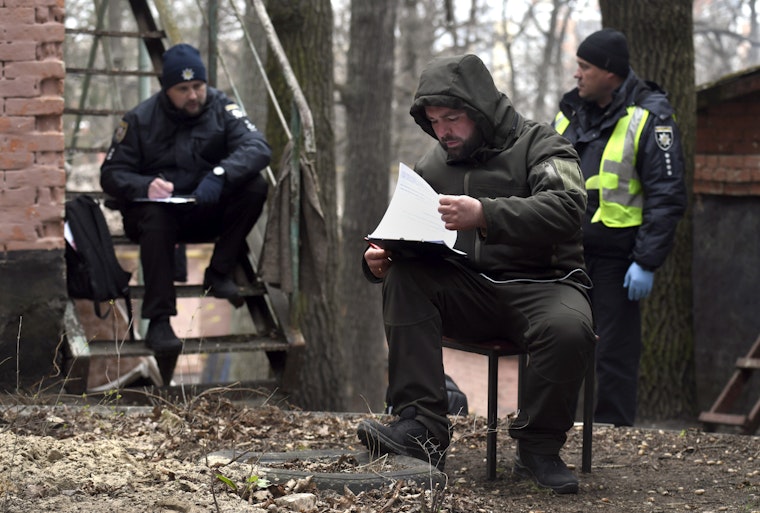 Police investigating war crimes in Irpin, Ukraine, on April 19, 2022. © Carol Guzy/Zuma/Newscom Three people outdoors, reviewing paperwork on a clipboard