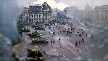 People walking around military tanks below damaged buildings