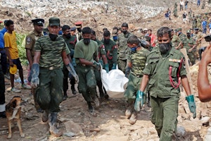 Men in uniforms carry a body away from a mountain of garbage