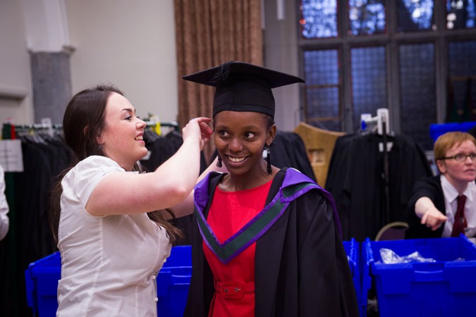 A woman helping another woman with a graduate robe