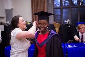 A woman helping another woman with a graduate robe