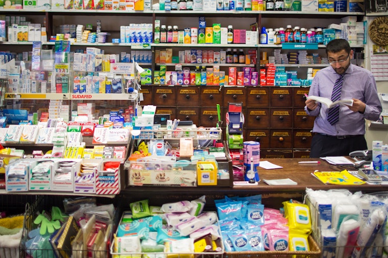 A pharmacist stands behind the counter in an independent pharmacy in Bath, England, on February 12, 2016. Photo credit: © Matt Cardy/Getty A man behind the counter at a pharmacy