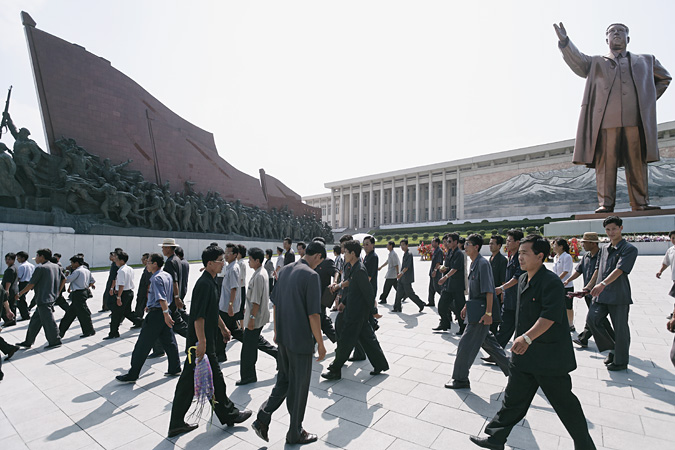People walking in plaza by statue of Kim Il Sung