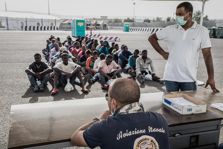 Recently arrived asylum seekers from North Africa await processing by Italian immigration authorities in Sicily on October 15, 2014. Photo credit: © Giles Clarke/Getty Men seated in rows