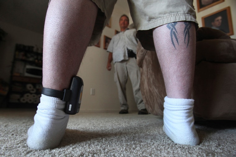 A parole agent talks with a man wearing a GPS locator on his ankle in Sacramento, California, on August 3, 2009. Photo credit: © Rich Pedroncelli/AP Legs of a man in socks on a carpet