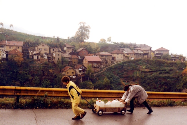 Two young people carting a wagon of water up a steep roadway