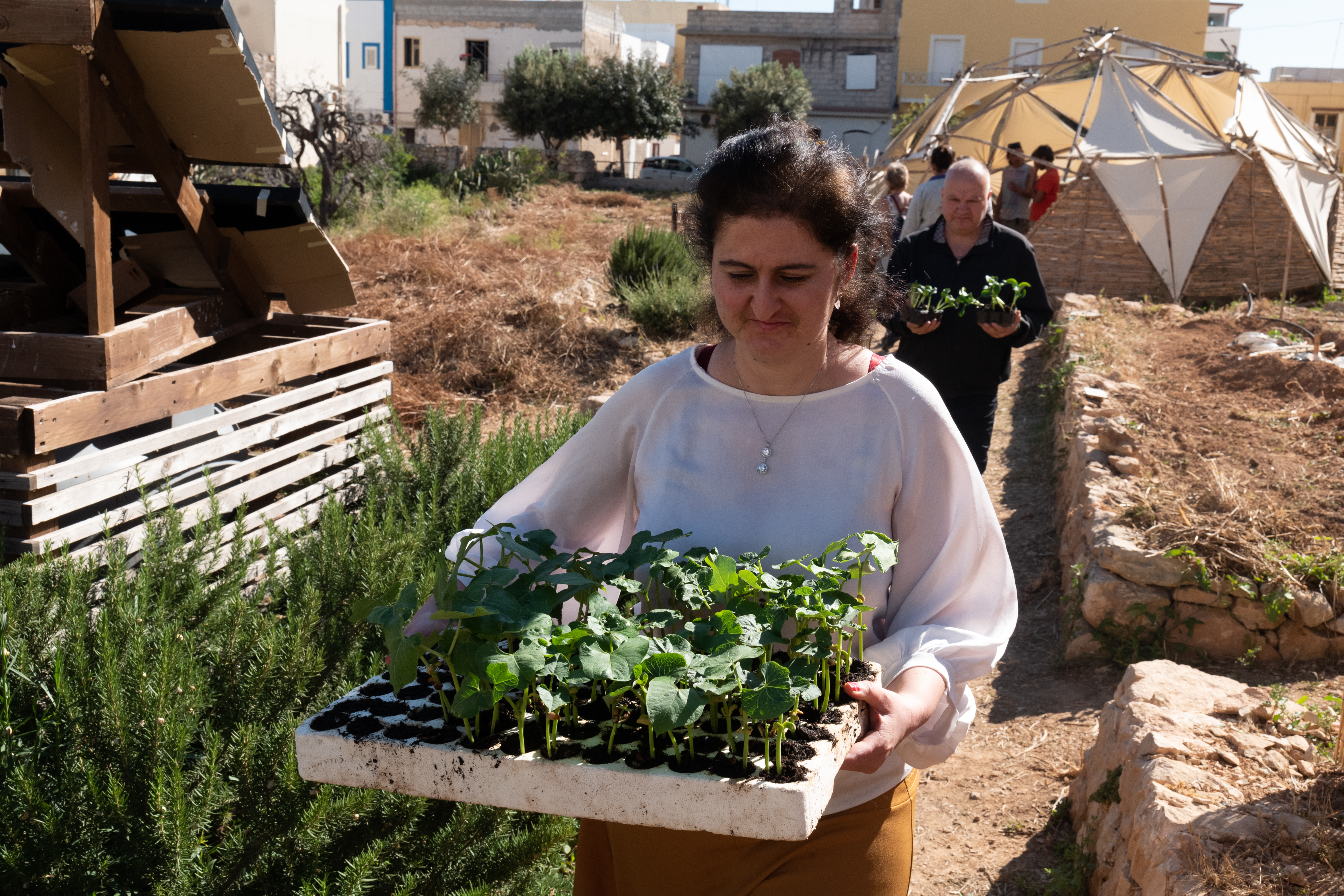 A woman carries plants in a garden