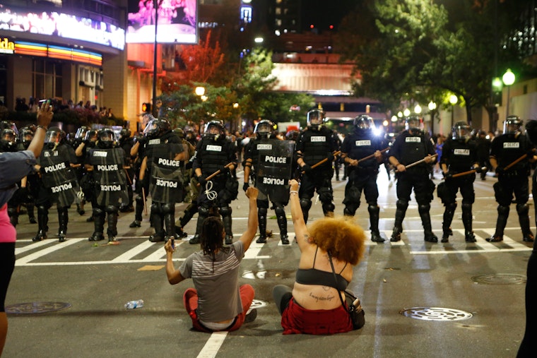 Activists protest the death of Keith Lamont Scott, who was shot and killed by the police, in Charlotte, North Carolina, on September 21, 2016. Photo credit: © Brian Blanco/Getty Two people sit in front of a row of police officers
