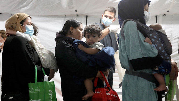 Evacuees from Afghanistan arrive at Tirana International Airport in Tirana, Albania, August 27, 2021. © Franc Zhurda/AP A woman standing in line with other women and holding a baby