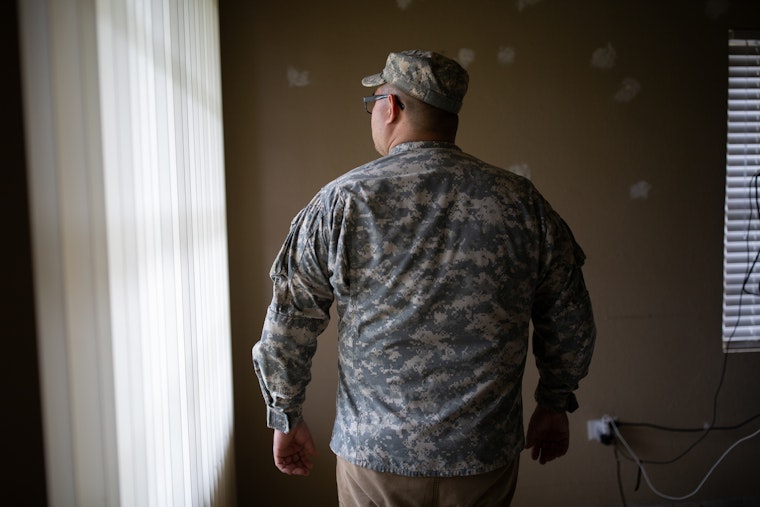 Diego (not his real name), a veteran, standing in his home, in Brownsville, Texas. Diego was born in Texas and has family on both sides of the U.S. border with Mexico. As an American citizen, crossing back and forth should be routine for him. In recent years, however, Diego has often been pulled aside by U.S. border officials, subjected to additional scrutiny, and told he will be placed in removal proceedings. Photo credit: © Griselda San Martin for the Open Society Foundations A man in a military uniform facing away from the camera