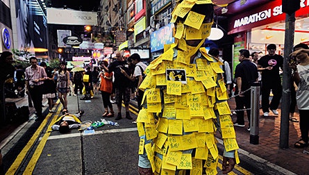 To commemorate the Tiananmen Square demonstrations 22 years earlier, a young artist has invited passers-by to cover him with notes of protest, many directed at the Chinese government and the Hong Kong leadership. Photo credit: © Mark Leong Man covered in notes