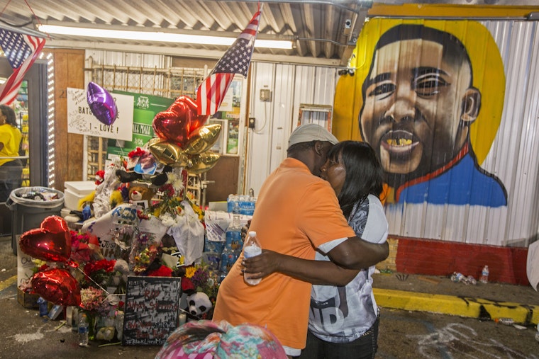 Two people embrace in front of a memorial