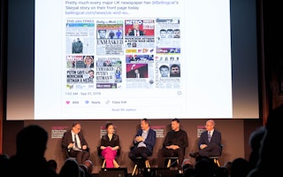 Five people seated on stage speaking below a projection of news stories
