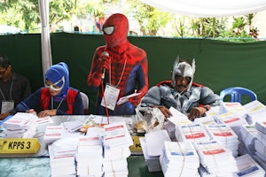 People dressed as superheroes behind stacks of ballots