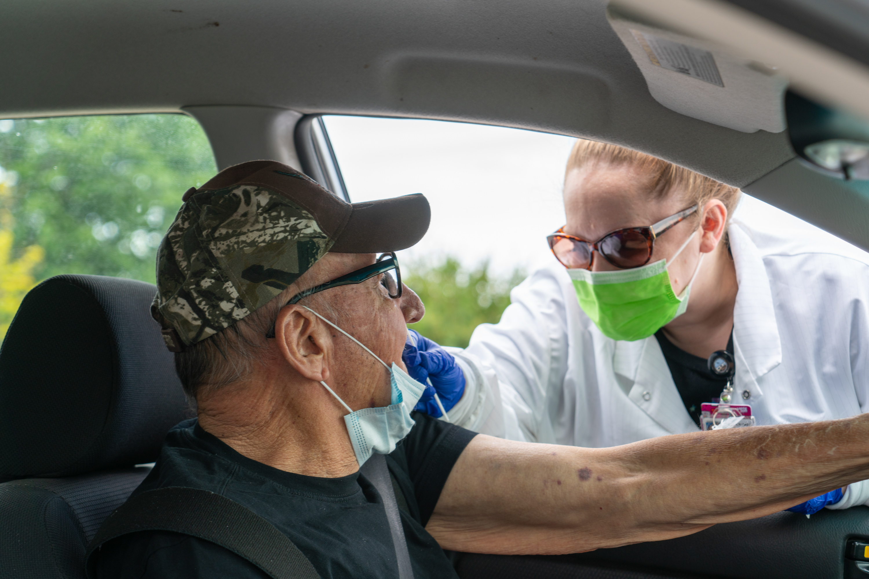 A person wearing a lab coat speaking to a driver through an open car window