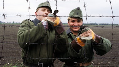 Two men using wire cutters to cut a razor wire fence.