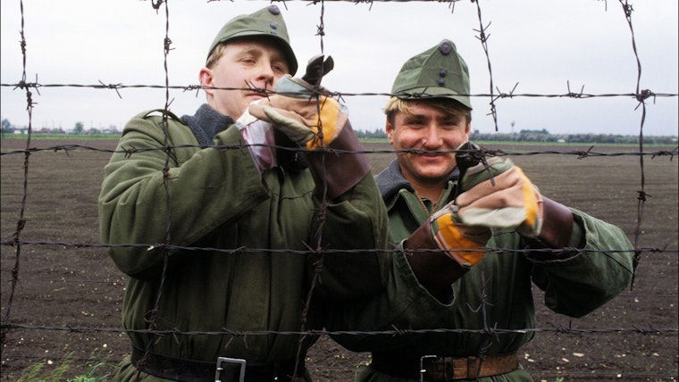 Two men using wire cutters to cut a razor wire fence.