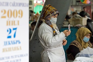 A market vendor uses her mobile phone next to an election poster in Tashkent, Uzbekistan, on December 24, 2009. Photo credit: © Shamil Zhumatov/Reuters Woman looking at her mobile phone