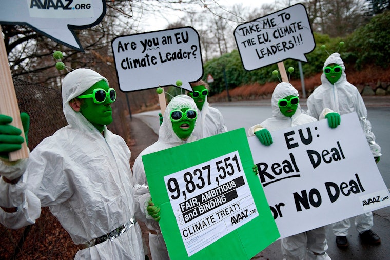 People wearing green face paint and costume antennae holding signs