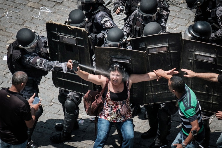 A riot police officer spraying a woman in the face with pepper spray