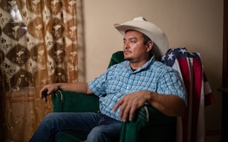 Alvaro (not his real name) poses with a cowboy hat and a U.S. flag in his home, in Los Fresnos, which is near Brownsville, Texas. Under the Trump administration, Alvaro’s mother was detained and interrogated by border officials—who coerced her into falsely claiming Alvaro was born in Mexico—and his wife’s green card was rejected. Photo credit: © Griselda San Martin for the Open Society Foundations A man in a cowboy hat sitting in an armchair