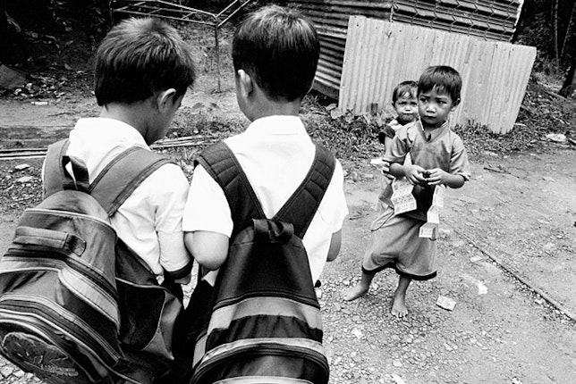 Two boys wearing backpacks; two smaller boys stand nearby