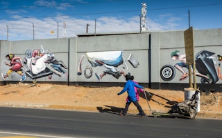 Trash pickers pull a cart past a mural