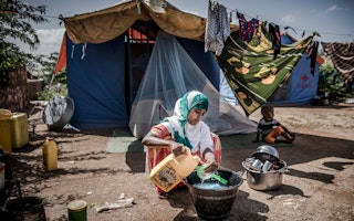 A woman washes dishes in a displaced persons camp.