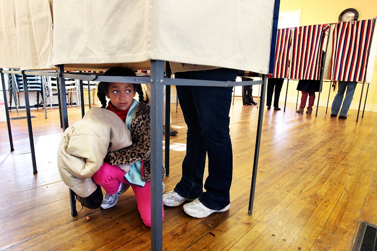 A girl crouching under a voting booth