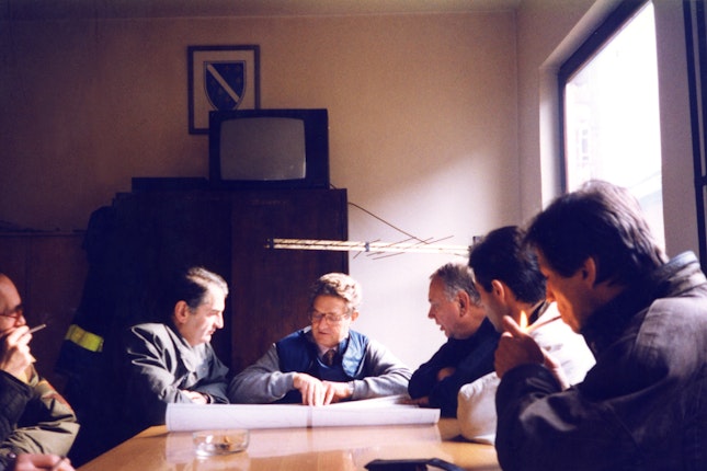 George Soros with a group of people looking over plan drawings
