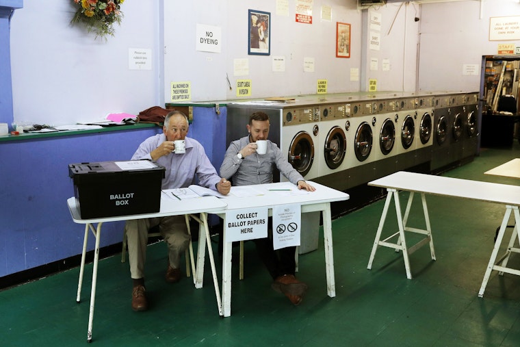 A presiding officer and a poll clerk drink a cup of tea while waiting for early morning voters at a polling station near Oxford, United Kingdom, on June 23, 2016. Photo credit: © Adrian Dennis/AFP/Getty Two people sit at a polling table in a laundromat