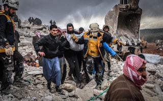 A group of people carrying an injured person among rubble