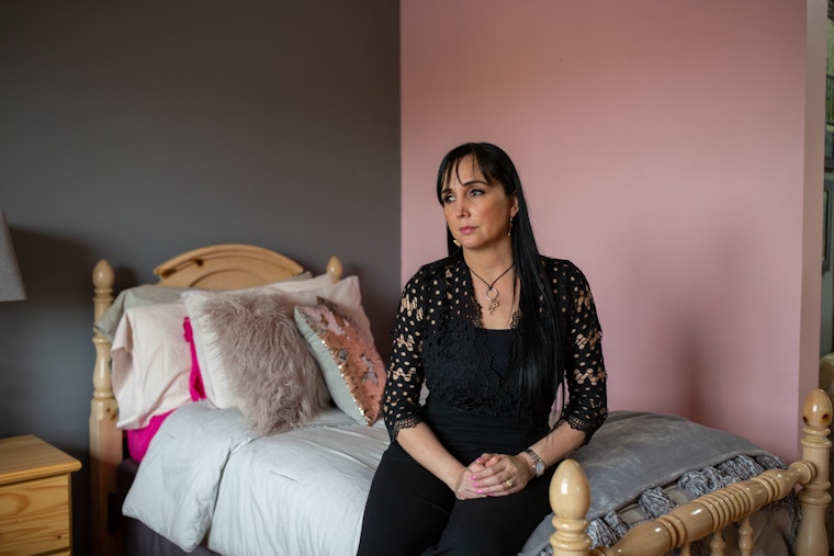 Raquel poses for a portrait in her daughters’ bedroom in Matamoros, Mexico, which is on the other side of the section of the border wall found in Brownsville, Texas. Because border officials have tried to question Raquel’s citizenship, her daughters have to cross the border every day if they want to stay enrolled in their school while also living with their mother. Photo credit: © Griselda San Martin for the Open Society Foundations A woman sitting on a bed